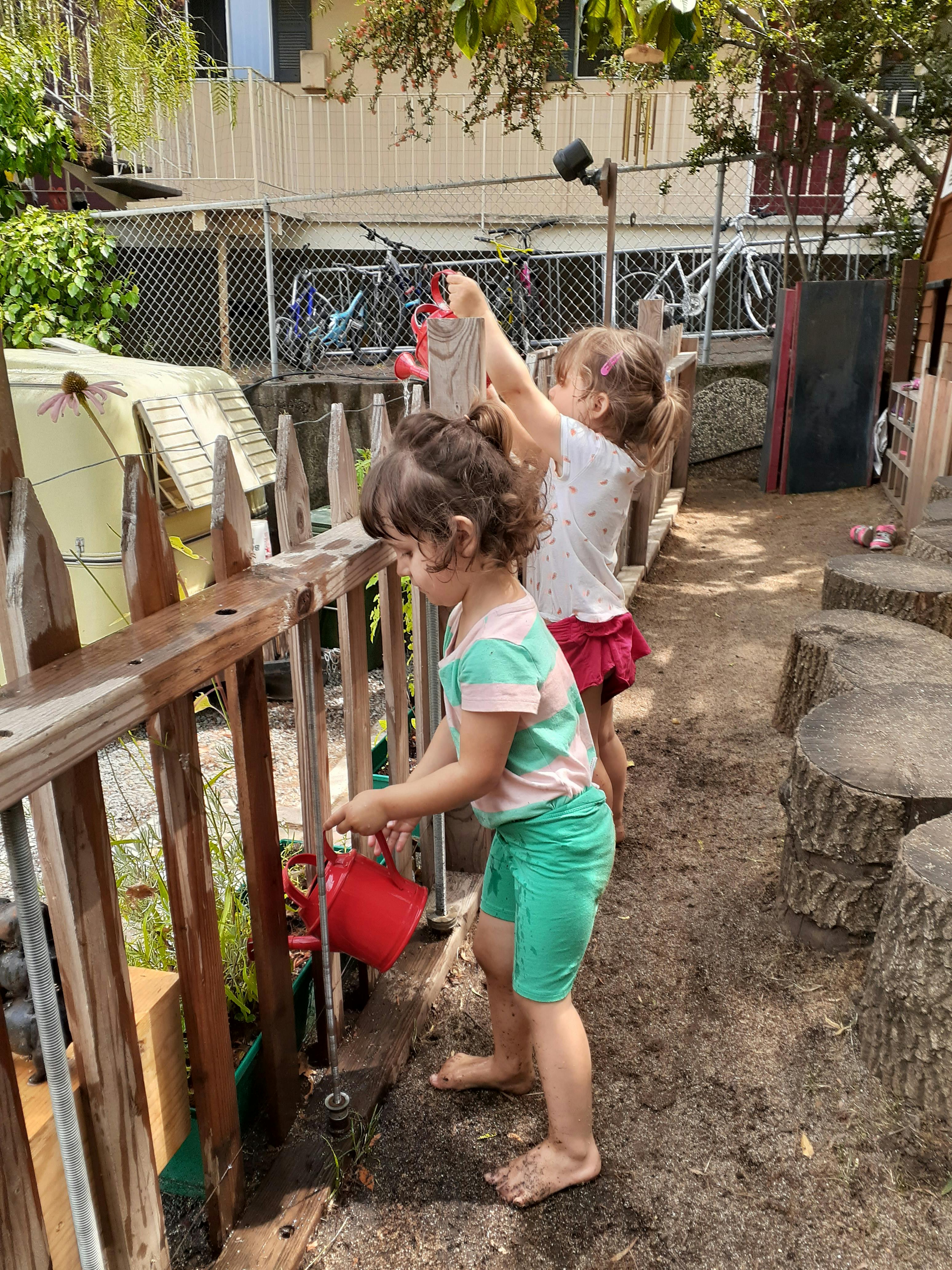 Two children playing with watering cans outdoors