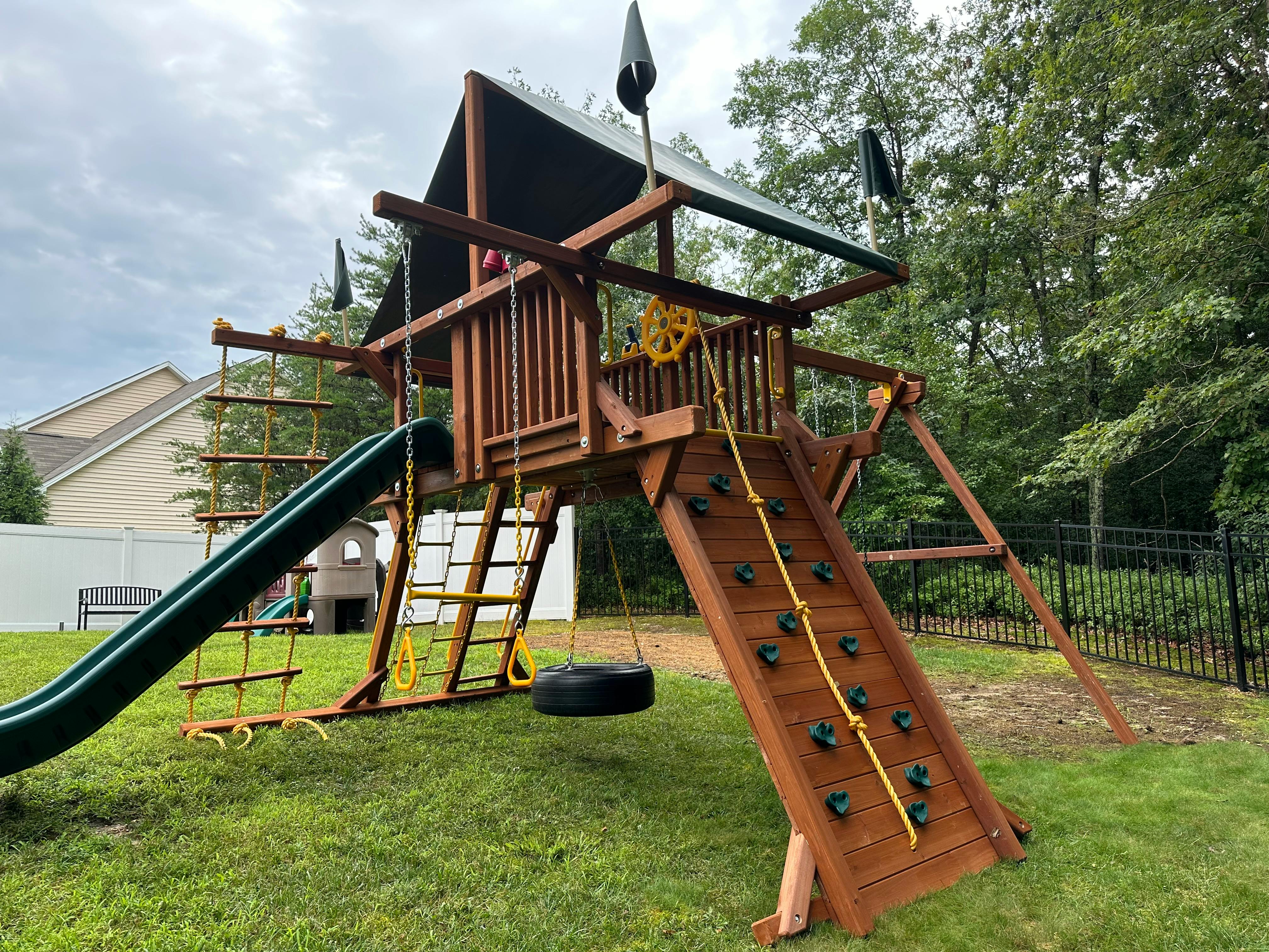 Wooden playset with slide, climbing wall, and tire swing
