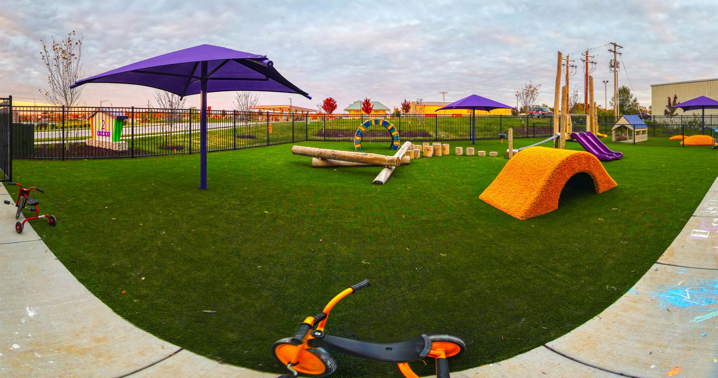 Outdoor playground with artificial turf, purple umbrellas, and various play structures