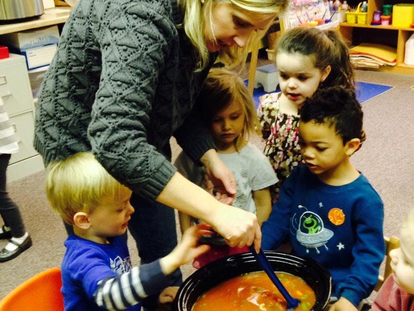 Adult and children gathered around a pot, stirring a liquid