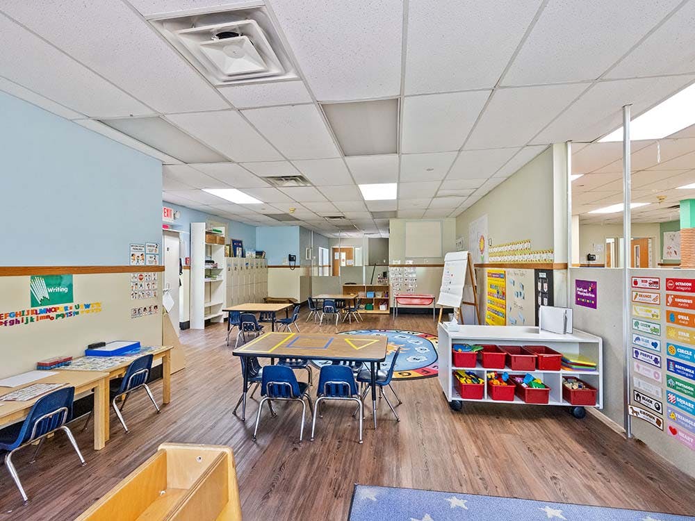 Empty classroom with small tables and chairs, whiteboards, and colorful learning aids