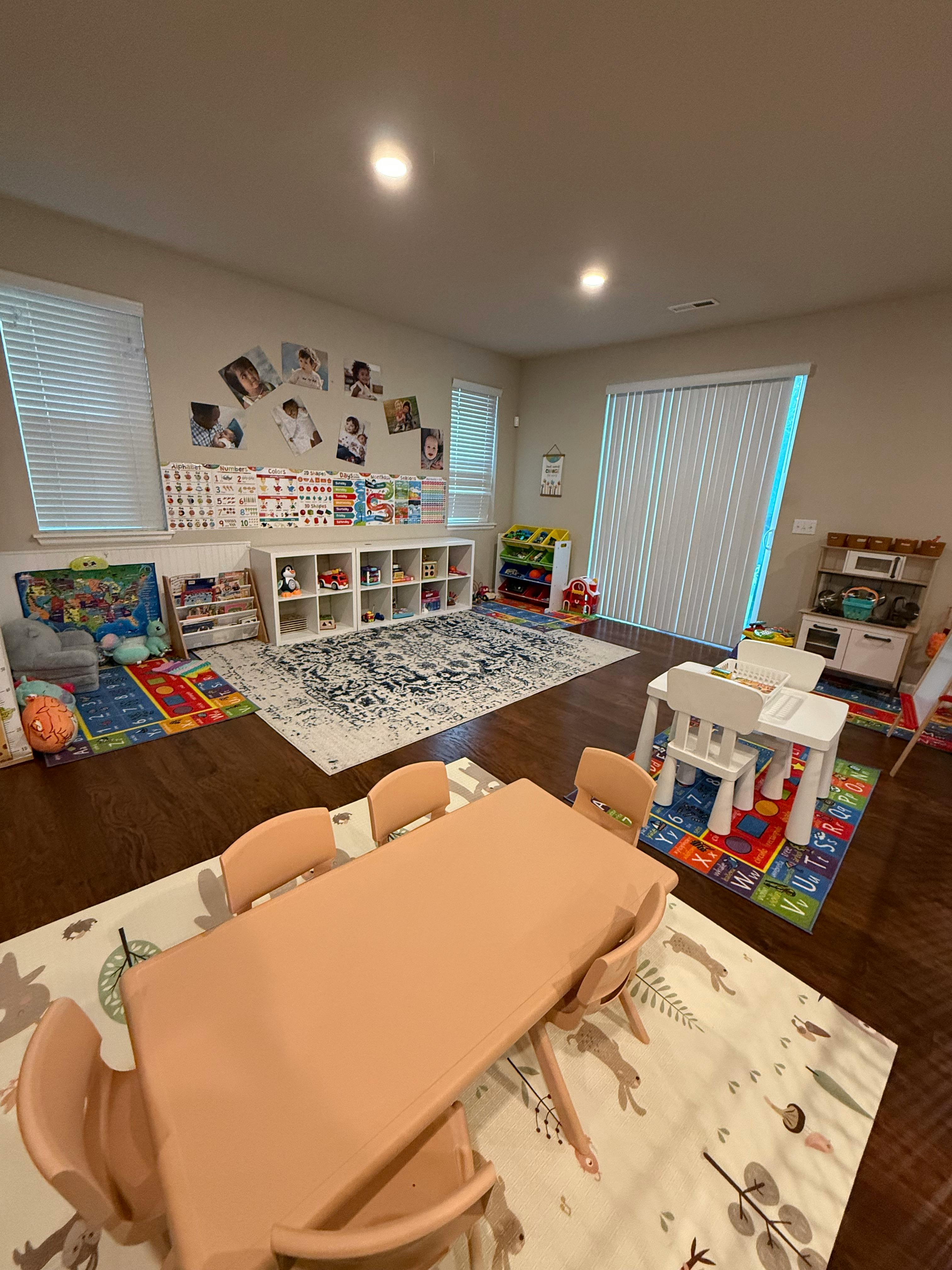 Playroom with multiple tables and chairs, rugs, and storage shelves with toys