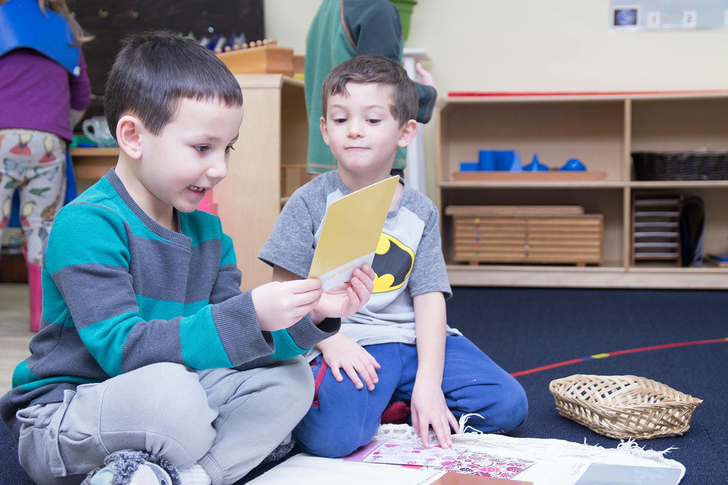 Two children sitting on the floor looking at a small card in a classroom