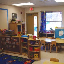 Classroom with small tables and chairs, shelves with toys