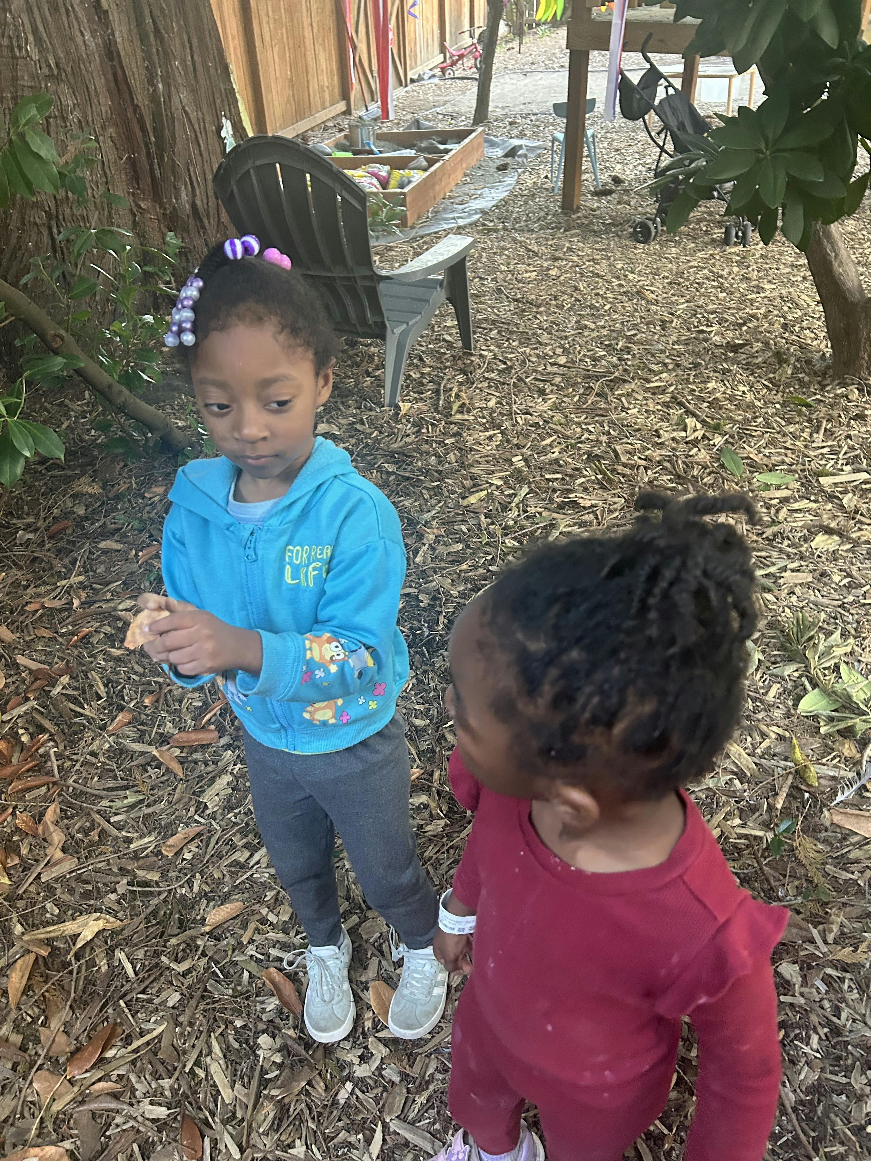 Two children standing in an outdoor area covered with wood chips
