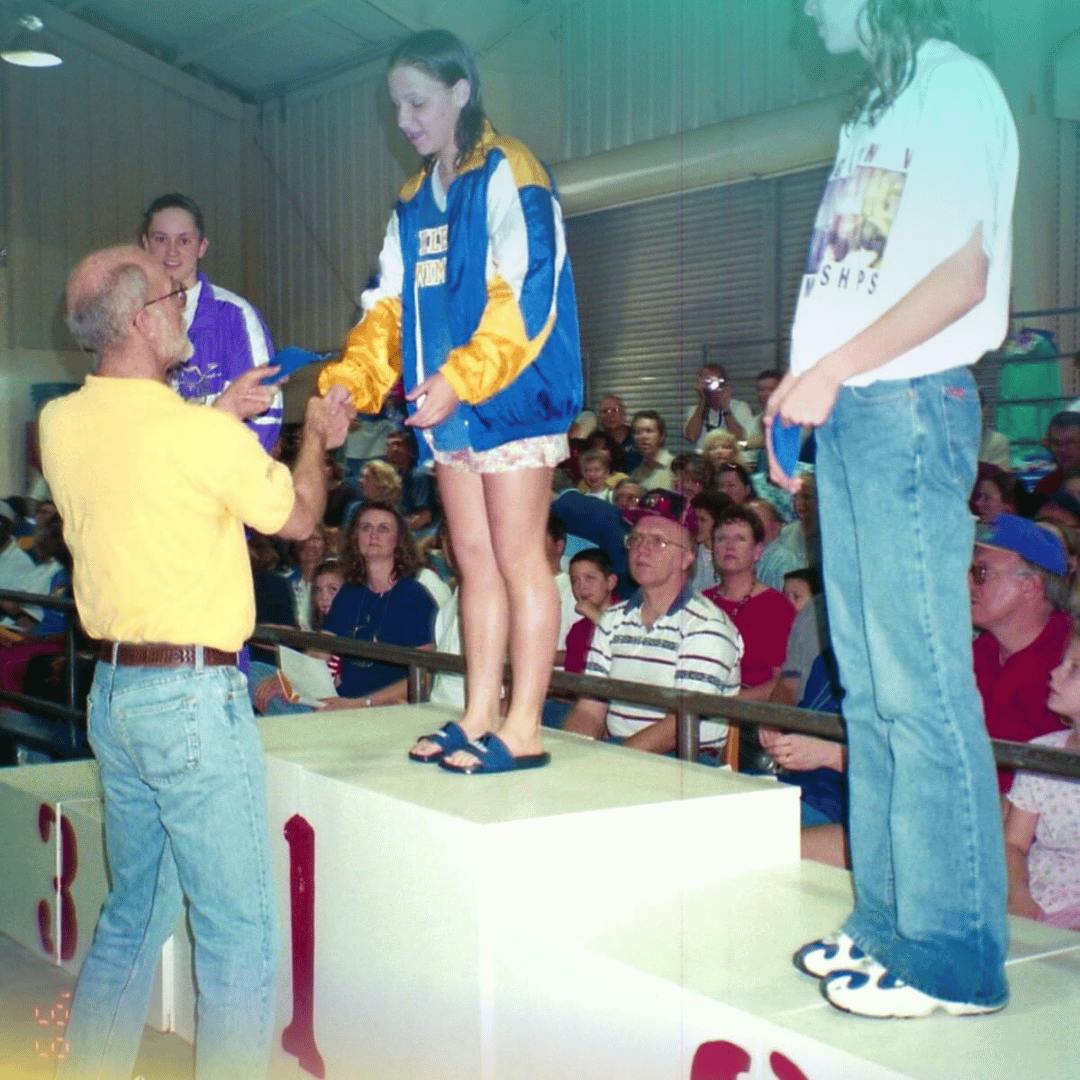 A person handing an award to a teen on a competition podium