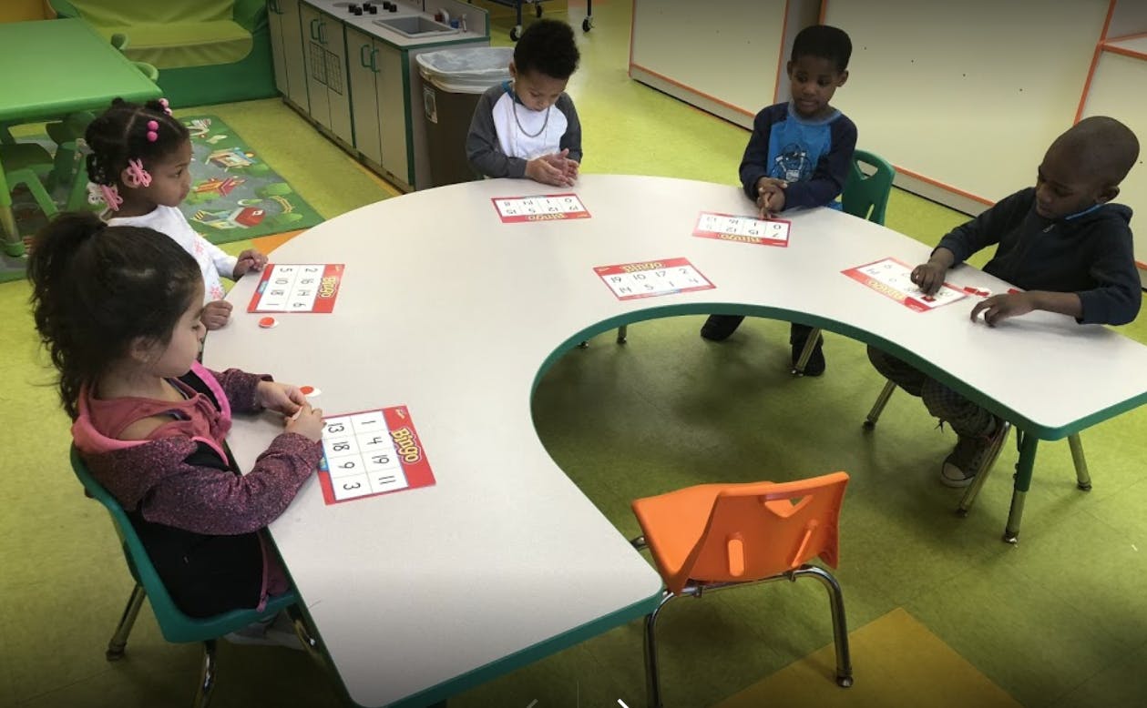 Four children sitting at a U-shaped table in a classroom