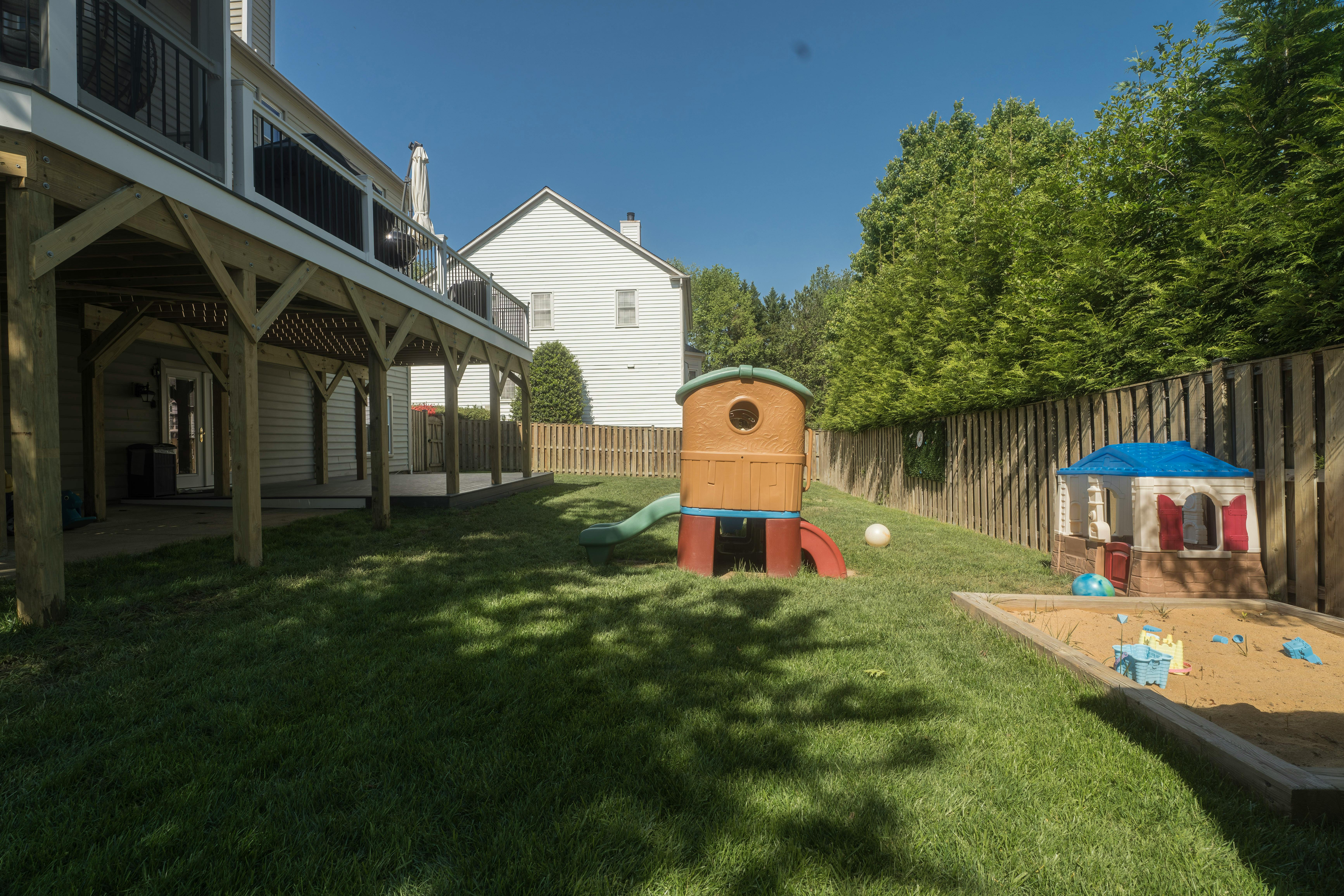 Backyard with a deck, playhouse, sandbox, and green grass