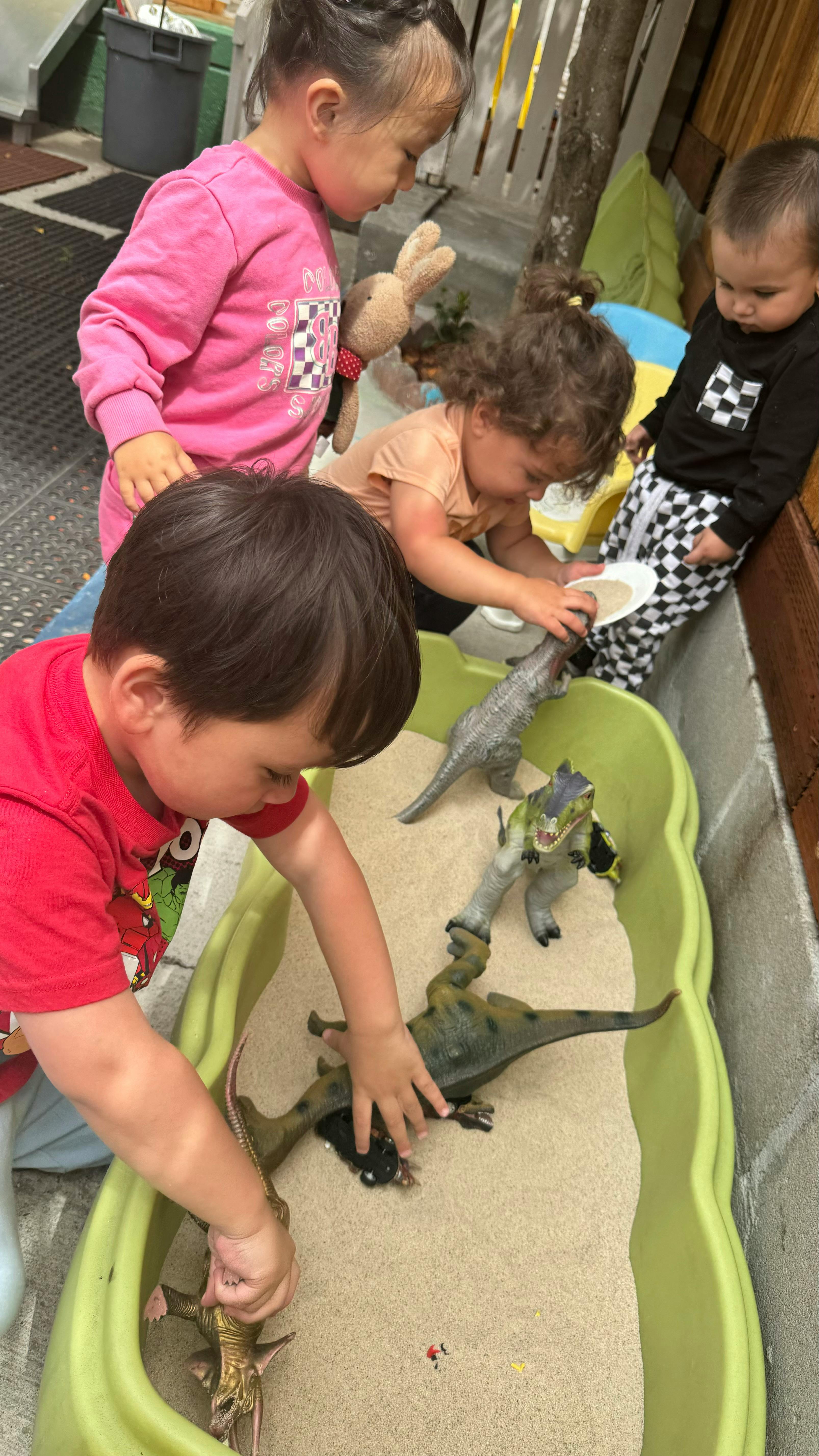 Children playing with dinosaur toys in a sand table