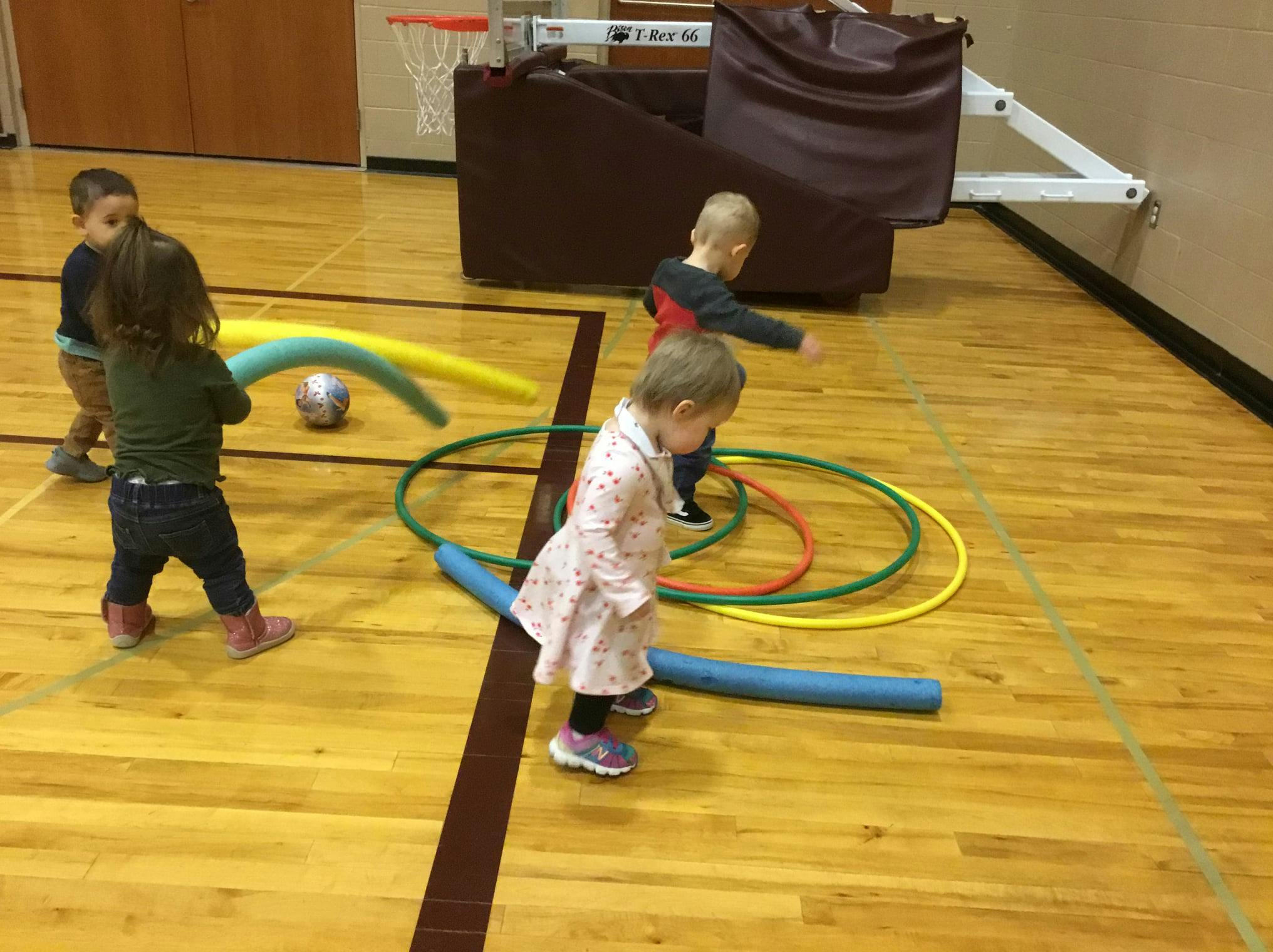 Children playing with hula hoops and pool noodles in a gym