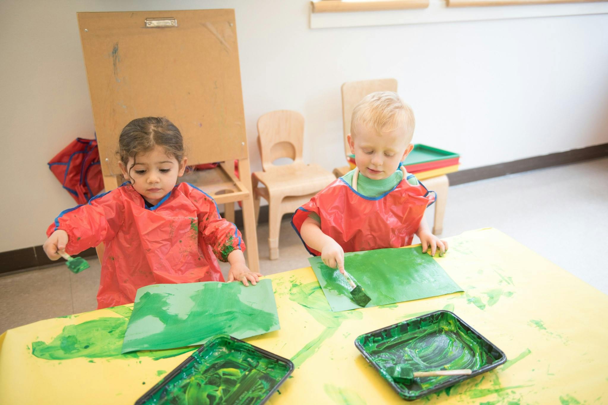 Two children painting with green paint at a table