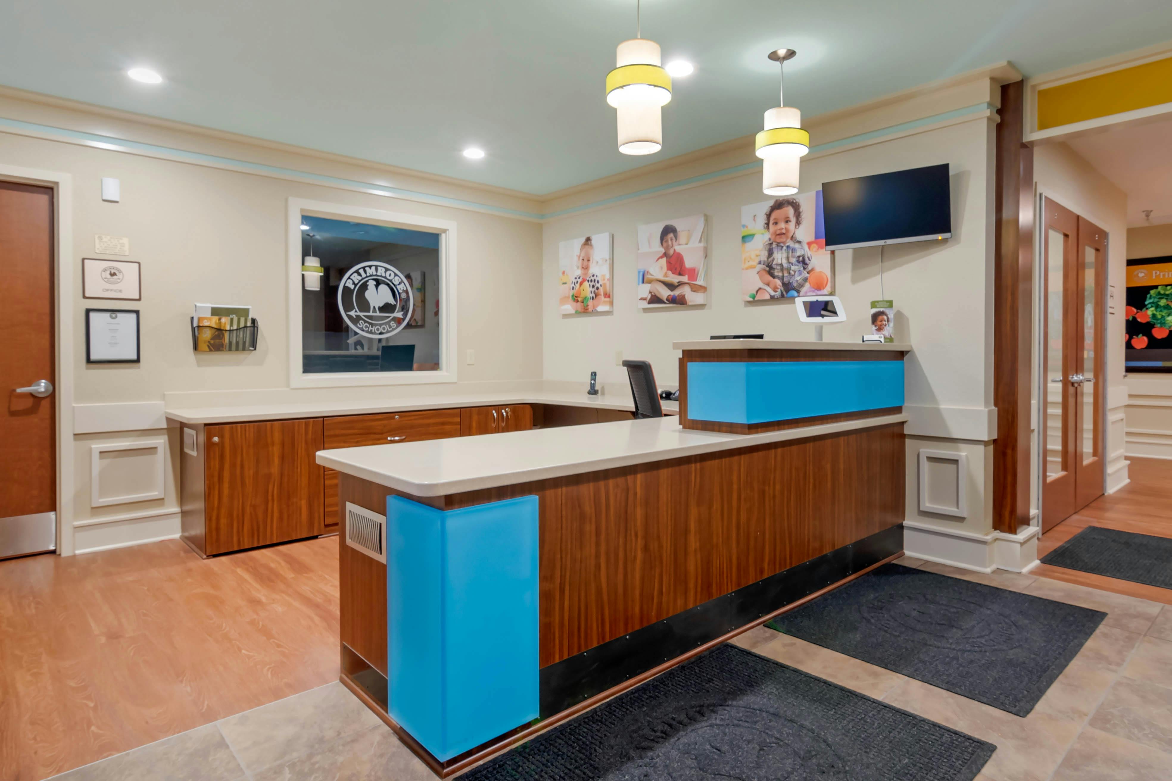 Reception desk with wood and blue panels, children's photos on wall, TV, and doors