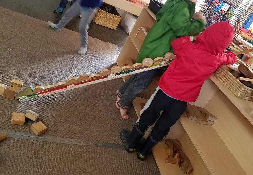 Two children playing with a long ramp and wooden blocks