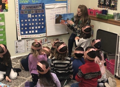 Person reading a book to a group of children in a classroom
