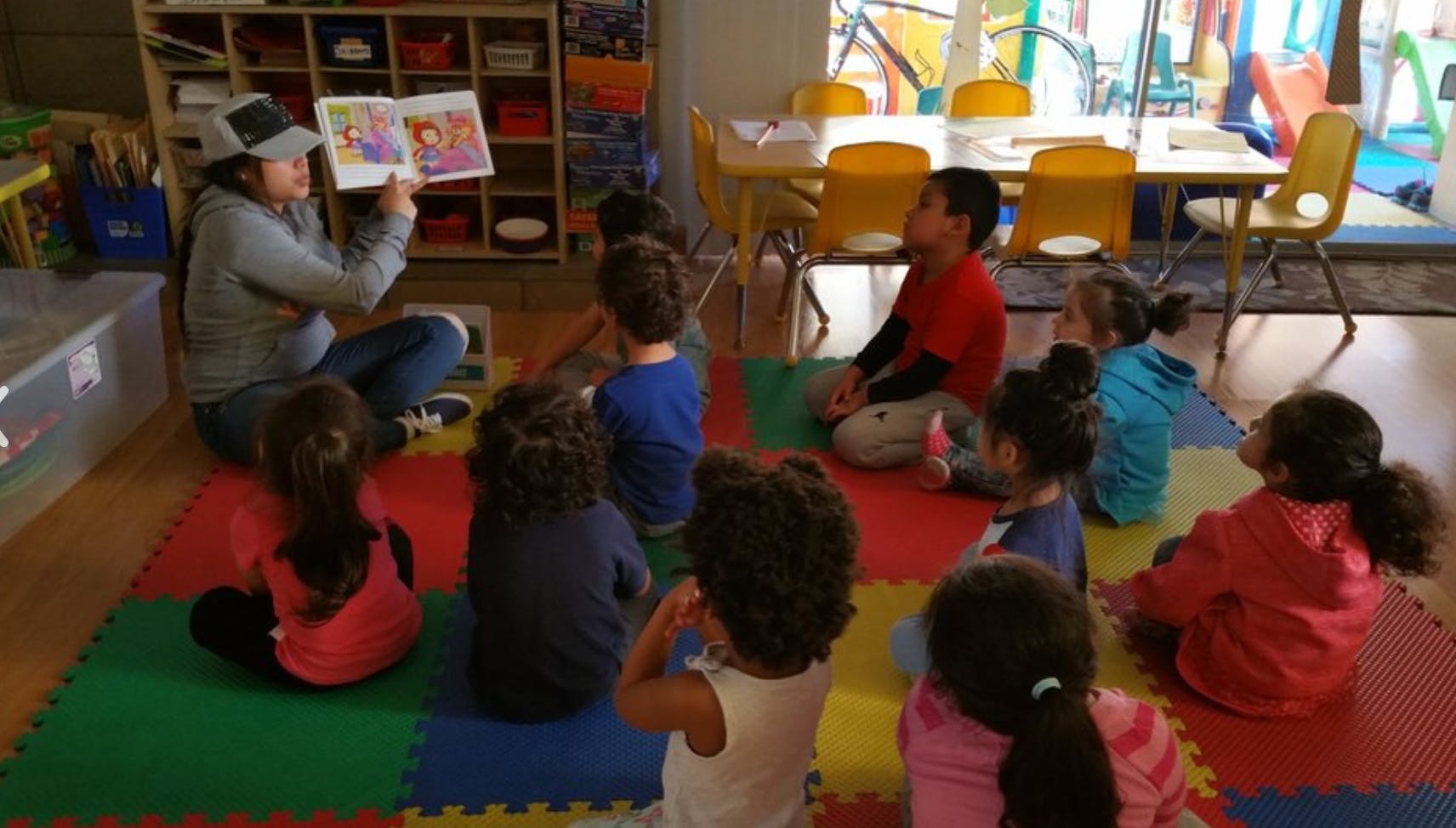 Person reading a book to a group of children in a classroom