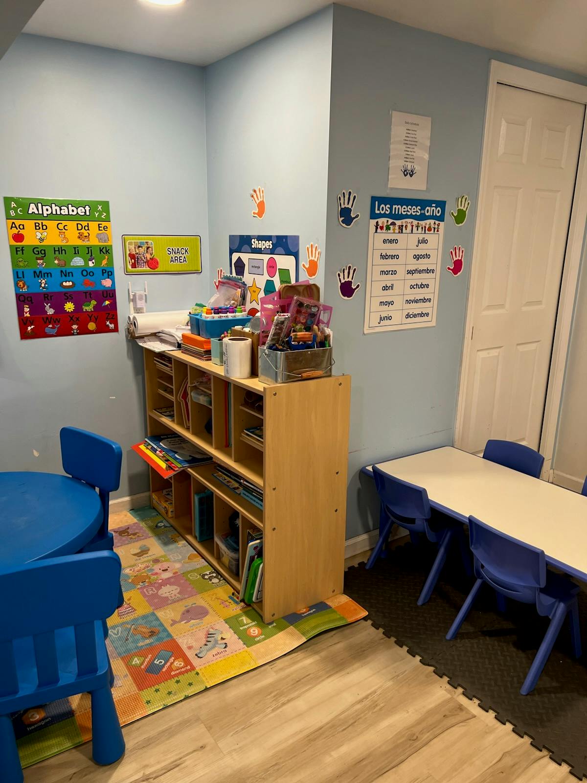 Classroom with small tables and chairs, shelving unit, and alphabet chart