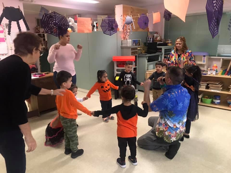 Adults and children in a classroom holding hands in a circle