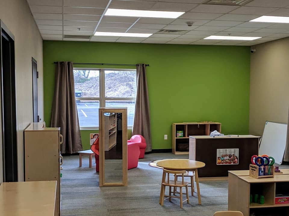 Empty classroom with green wall, window, and small tables and chairs