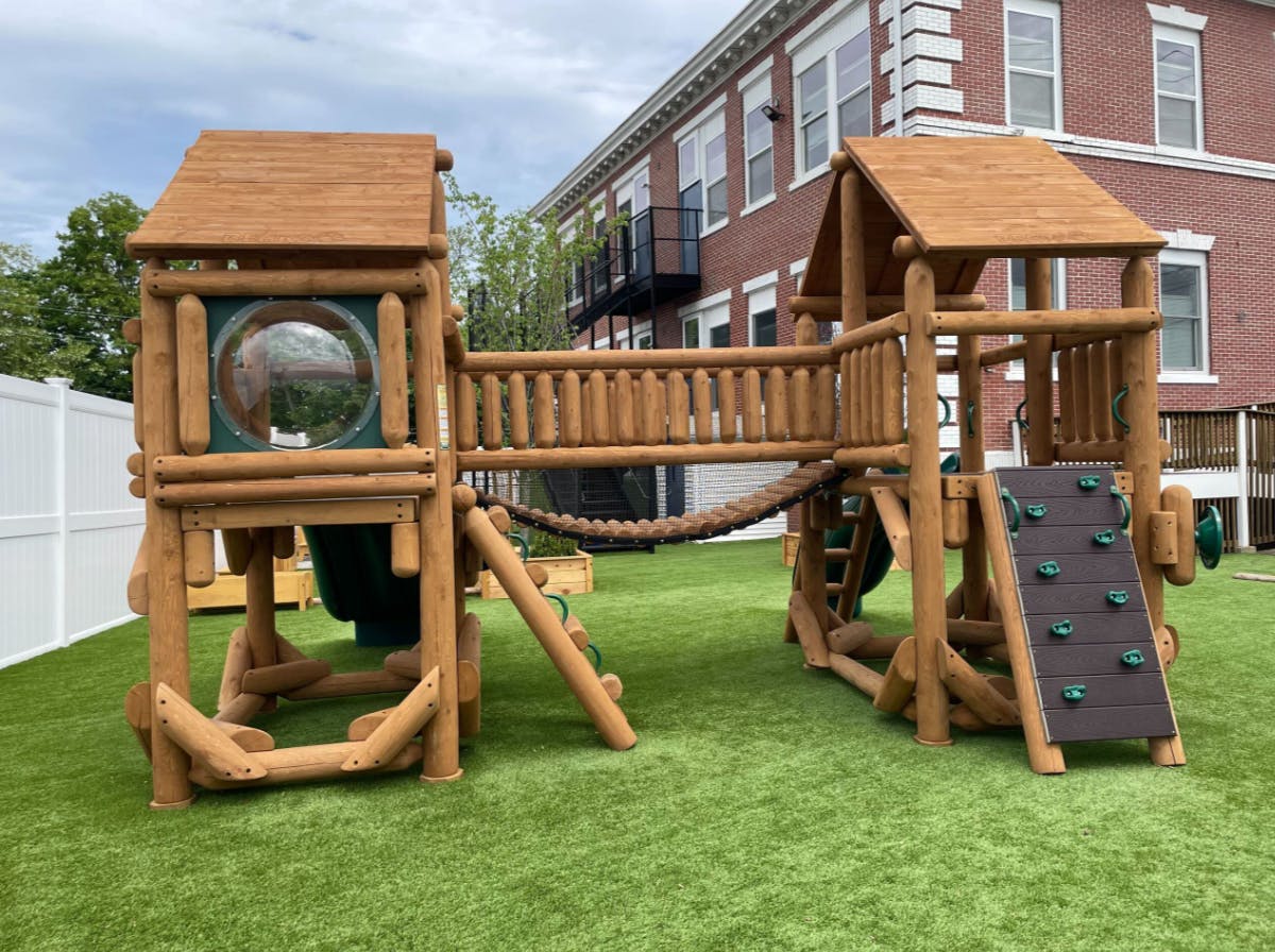 Wood playground structure with a bridge and climbing wall on artificial grass