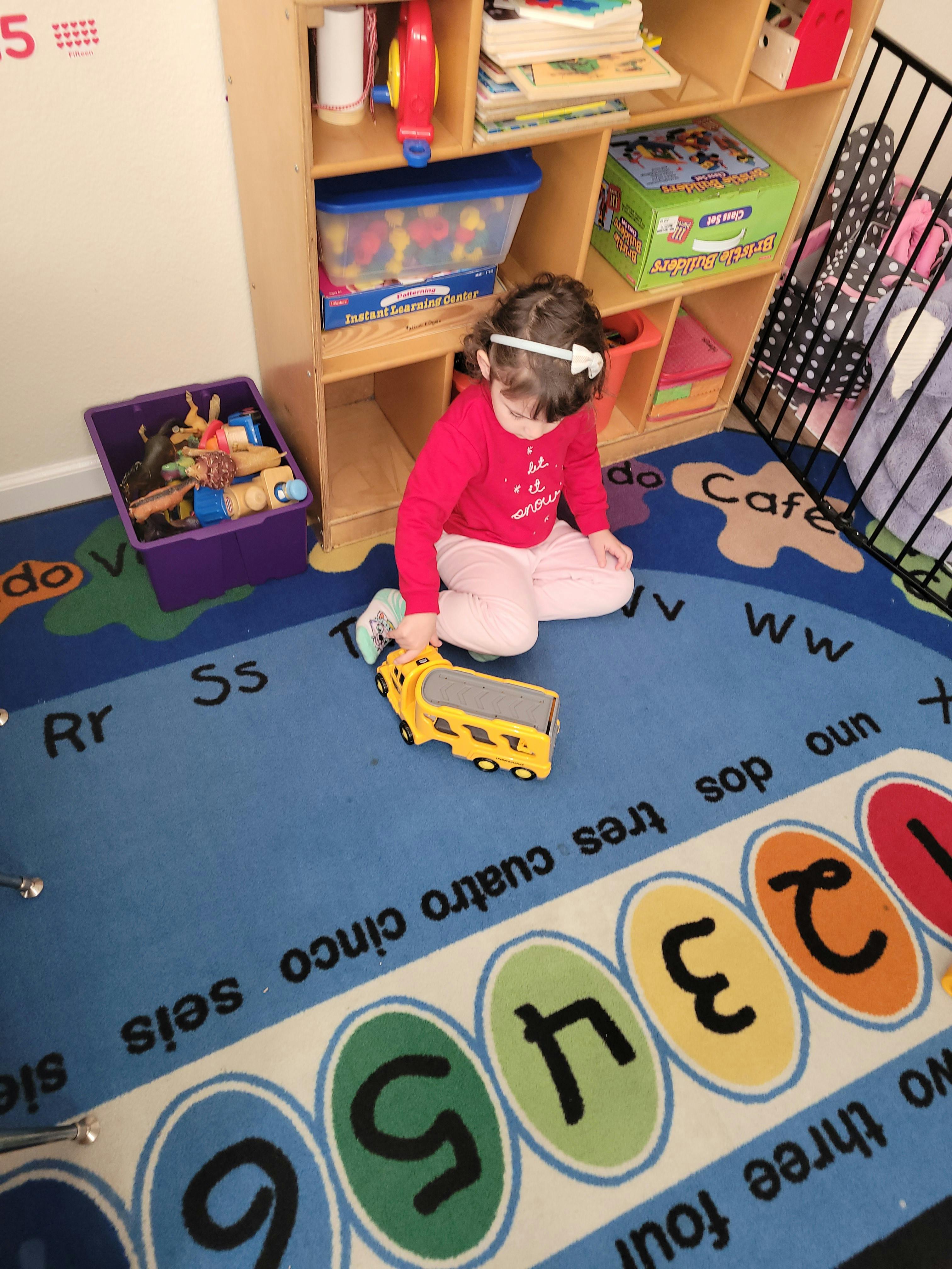 Child sitting on an educational rug playing with a yellow toy vehicle