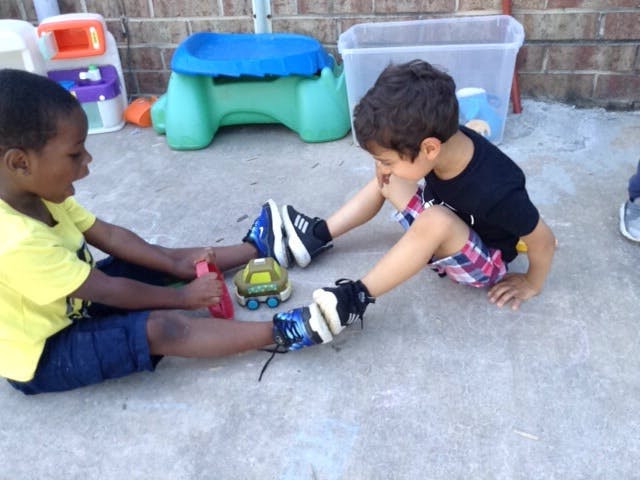 Two children sitting on the ground playing with a toy car