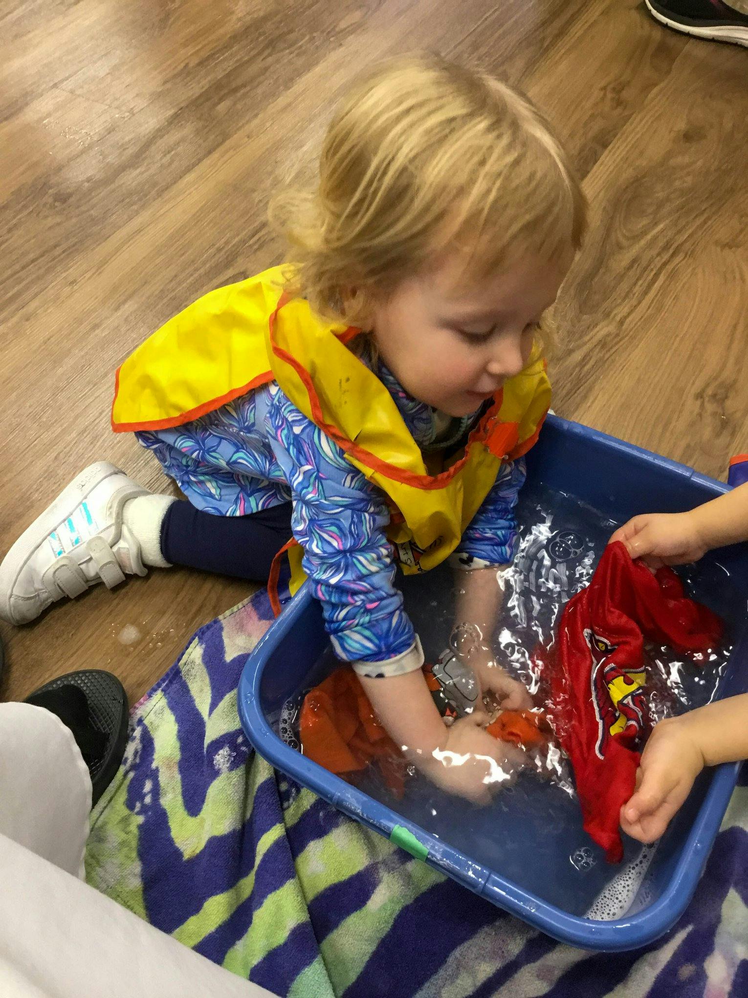 Child in a yellow smock playing with water in a blue bin