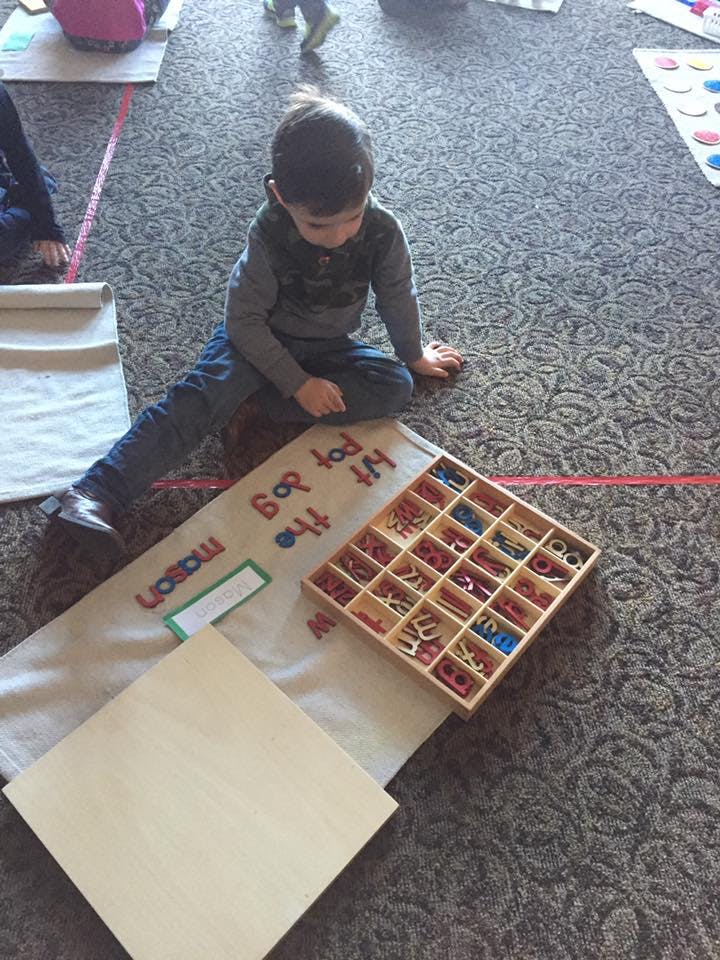 Child sitting on floor with letter tiles and a mat with words