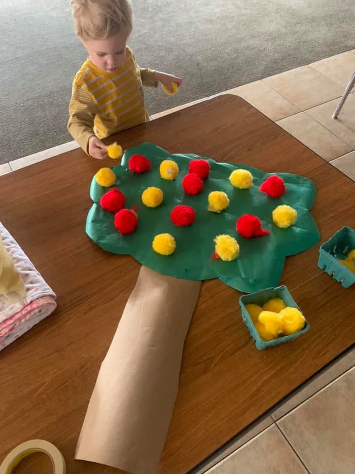 Child playing with pom-poms on a tree-shaped mat