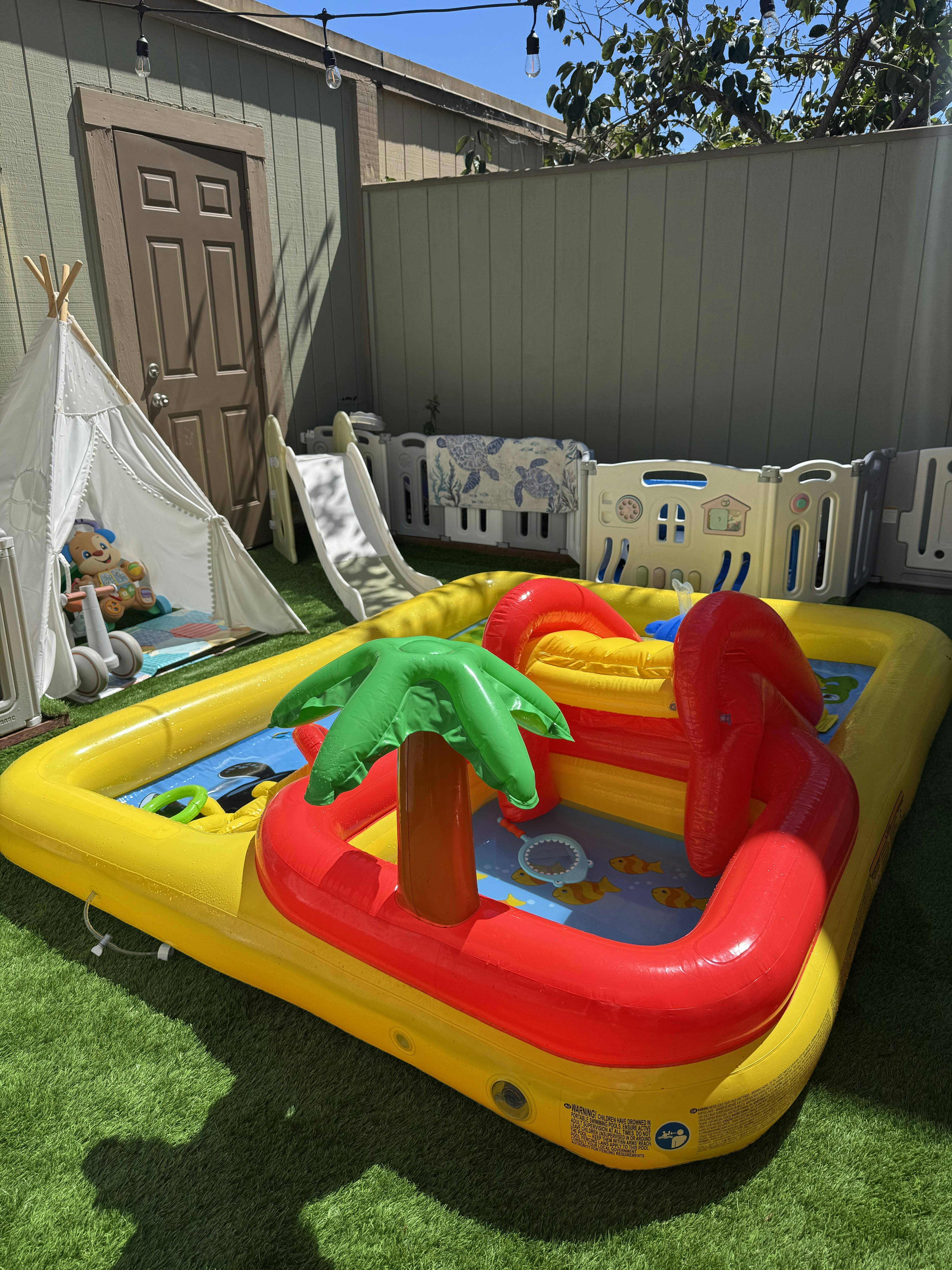 Inflatable kiddie pool with a palm tree and slide in a backyard