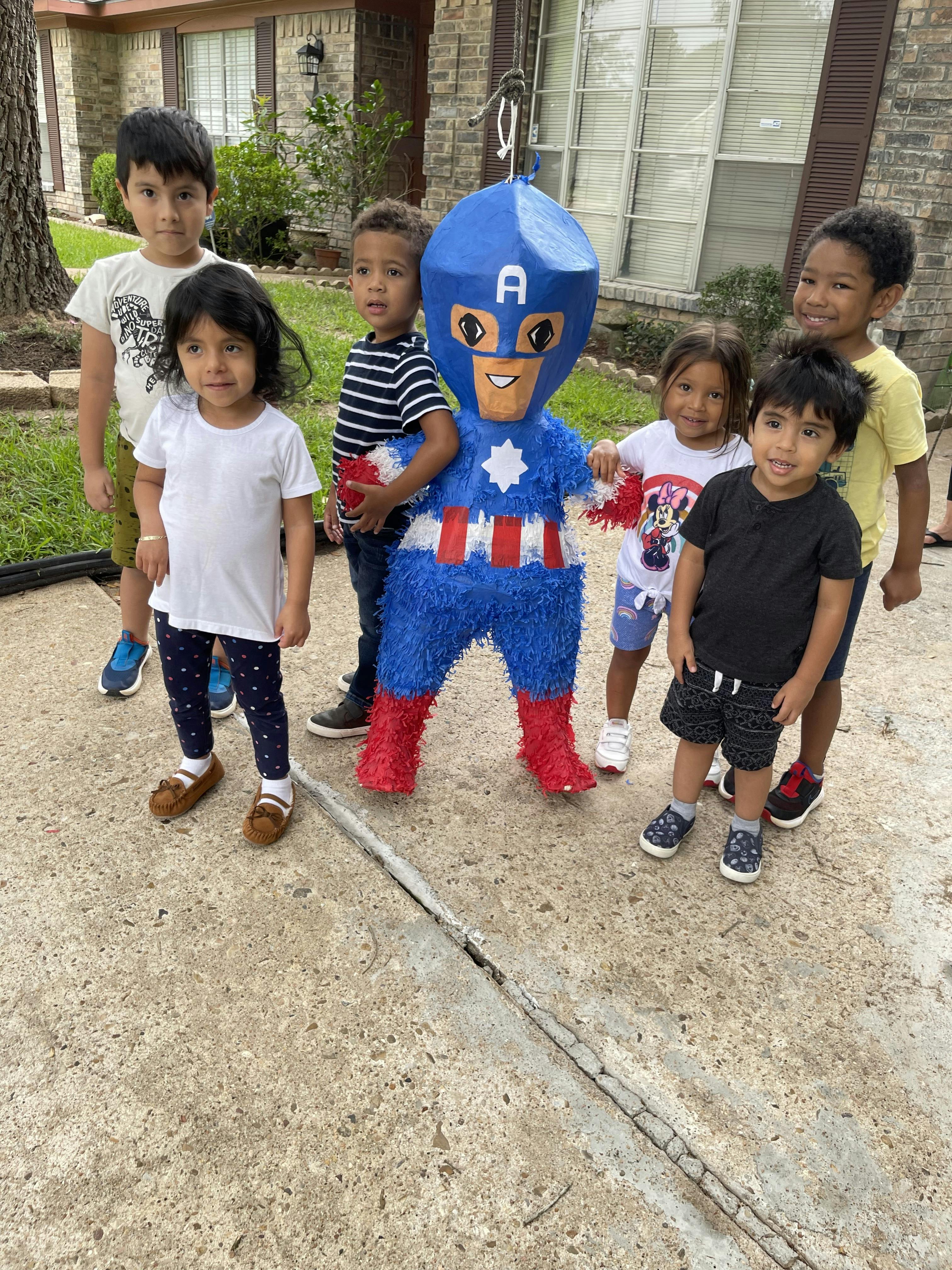 Children standing around a Captain America piñata