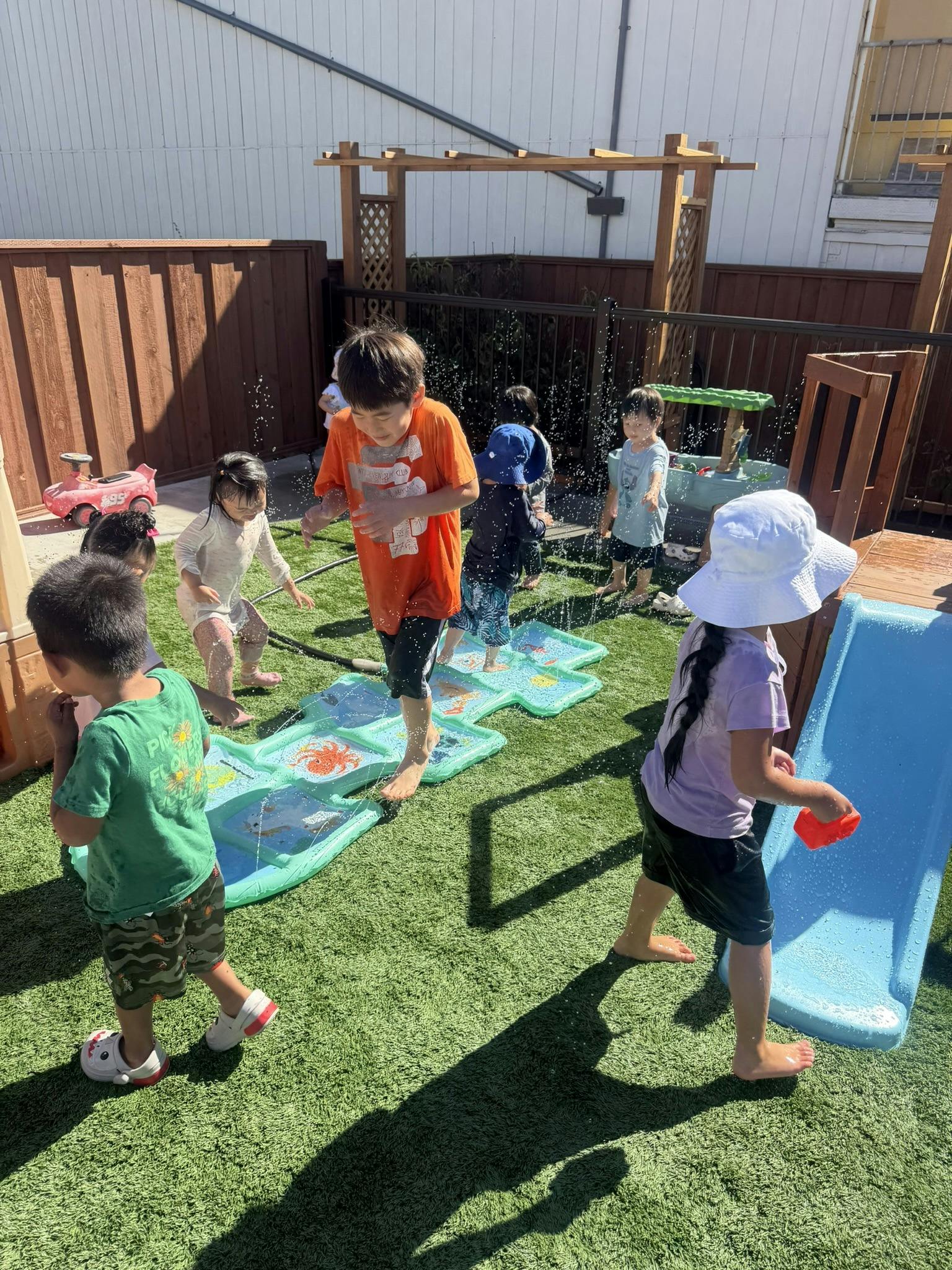 Children playing in a backyard with a water sprinkler mat and slide