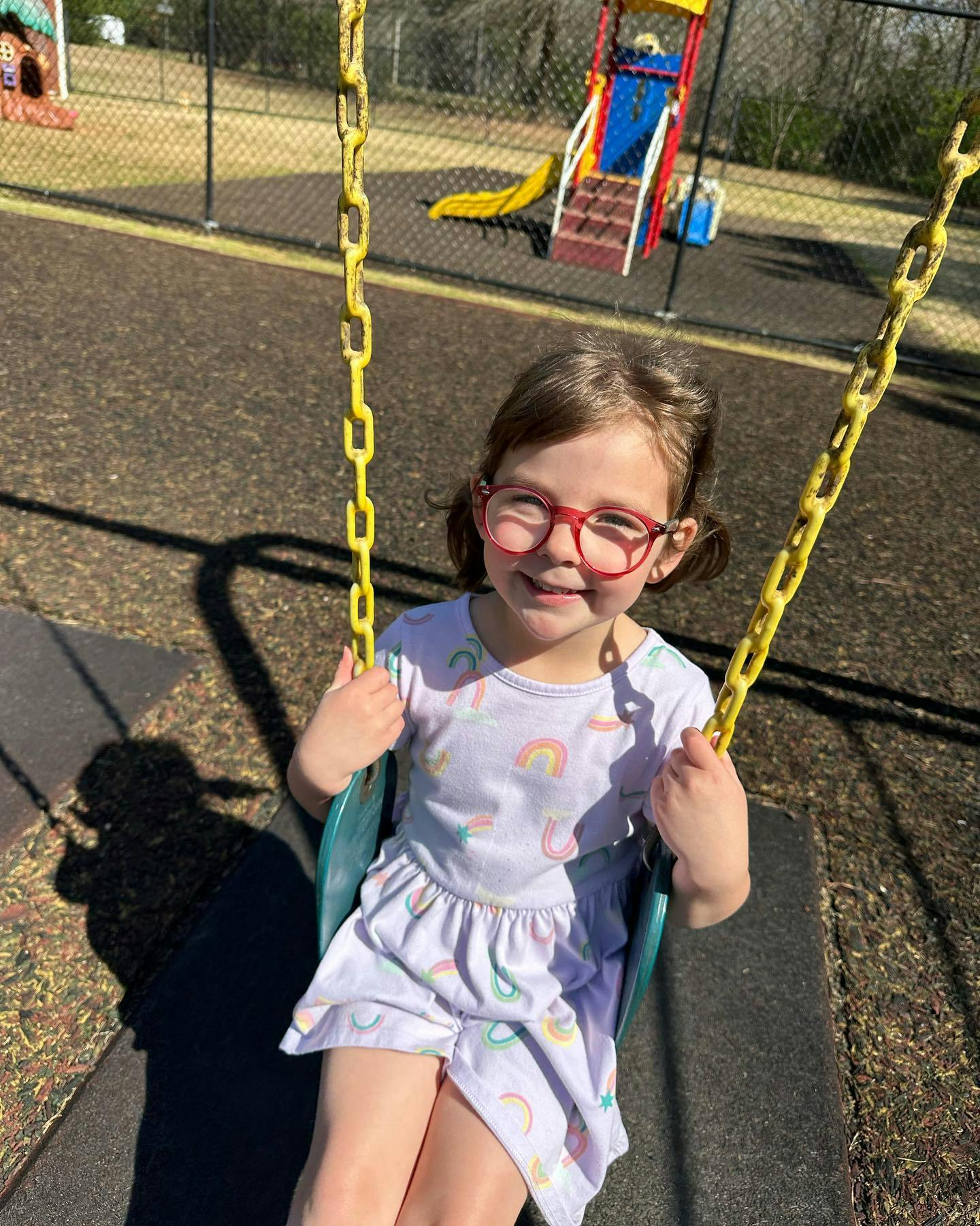 Child with red glasses sitting on a swing at a playground