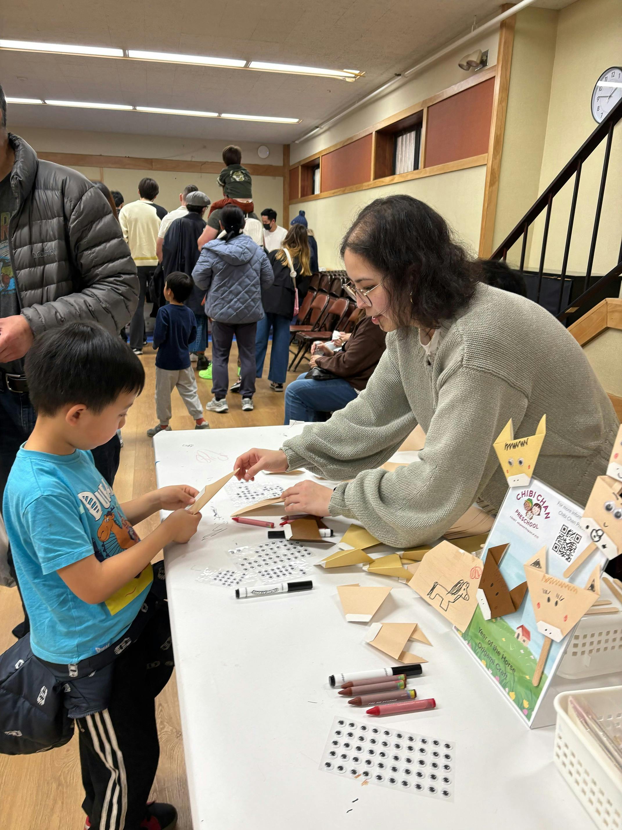 A person and a child at a table making paper crafts with googly eyes
