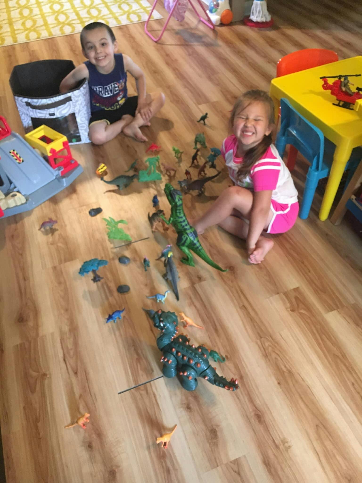 Two children playing with dinosaur toys on a wooden floor