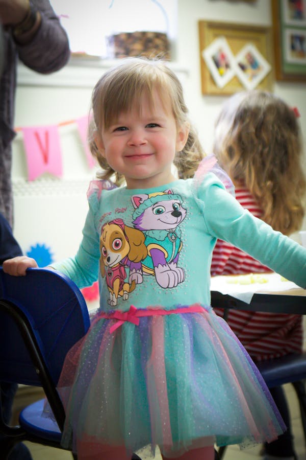 Child in a blue shirt with cartoon characters and a colorful tutu