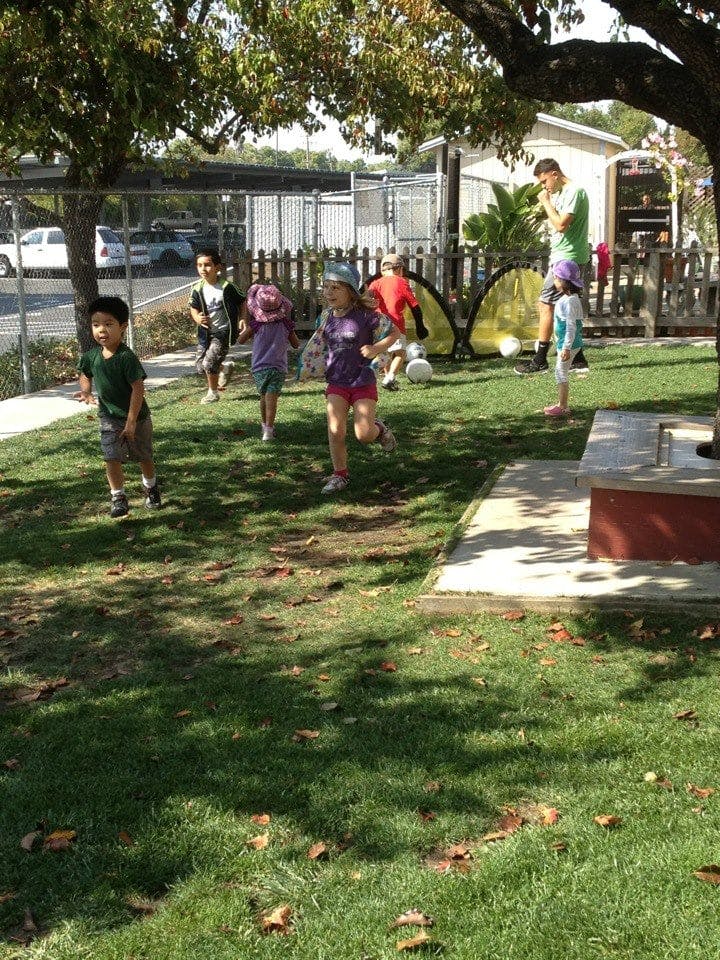 Children running on grass with an adult standing in the background