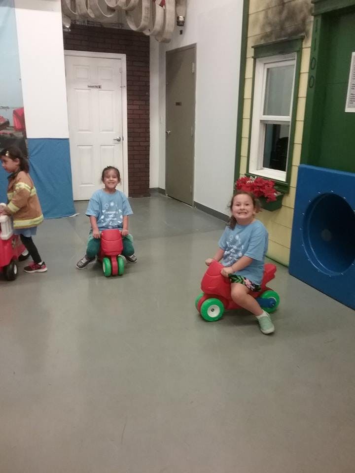 Three children riding toy vehicles indoors