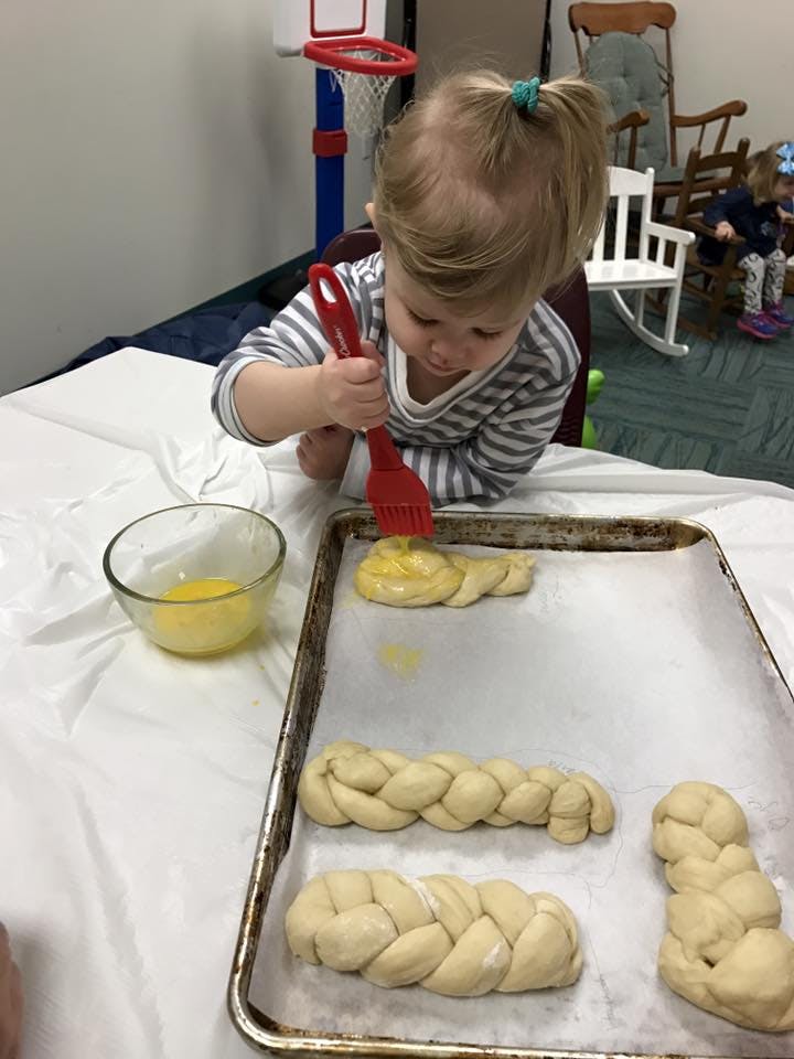 Child brushing egg wash on braided dough on a baking sheet