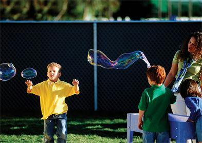 Child playing with bubbles outdoors with other children and an adult nearby