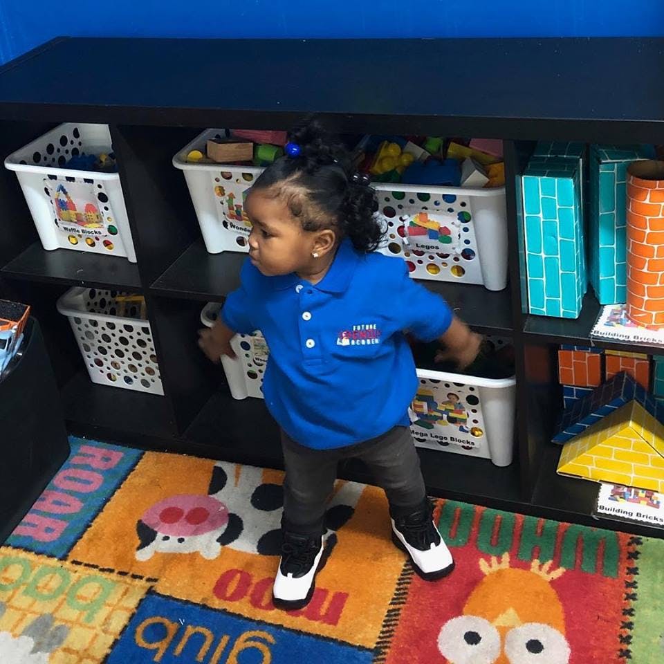 Child standing on a colorful rug in front of shelves with toys