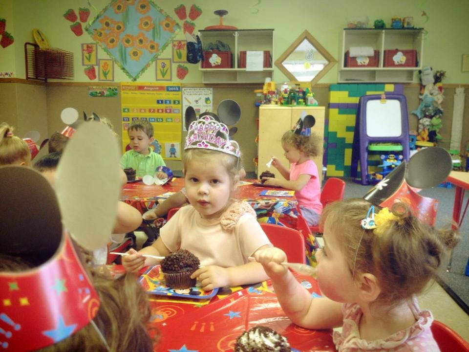 Child in a crown eating a cupcake at a table with other children