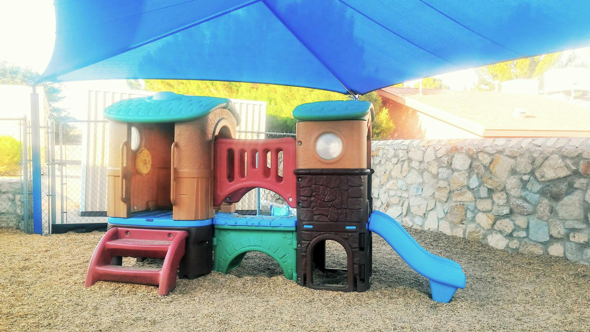 Playground structure with slide under a blue shade canopy
