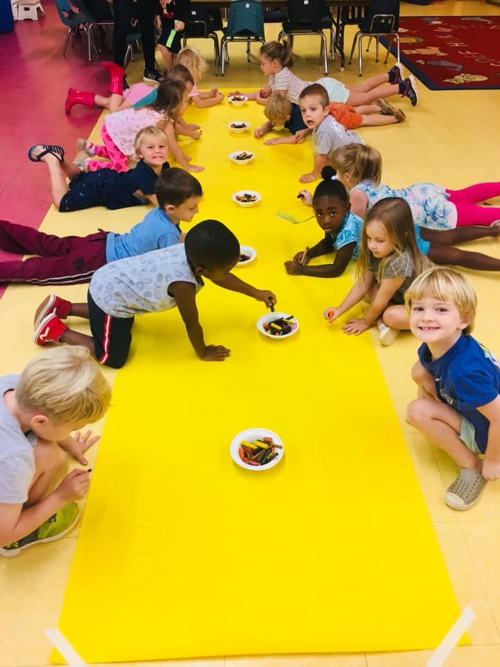 Children lying on a yellow mat reaching for items on small plates