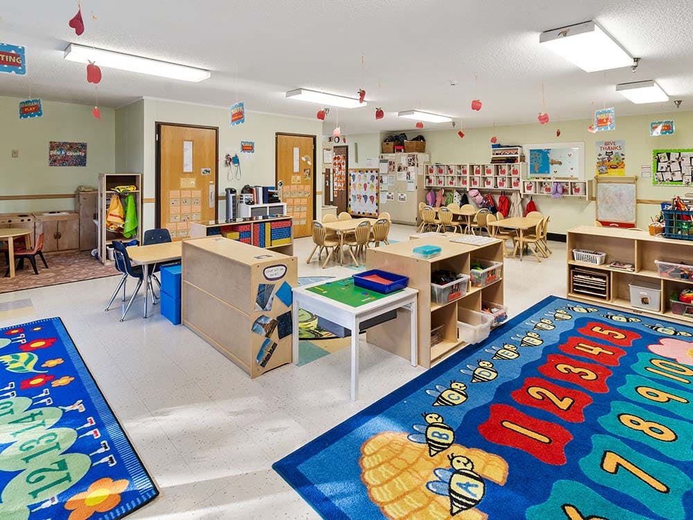 Empty colorful preschool classroom with small tables, chairs, and play areas