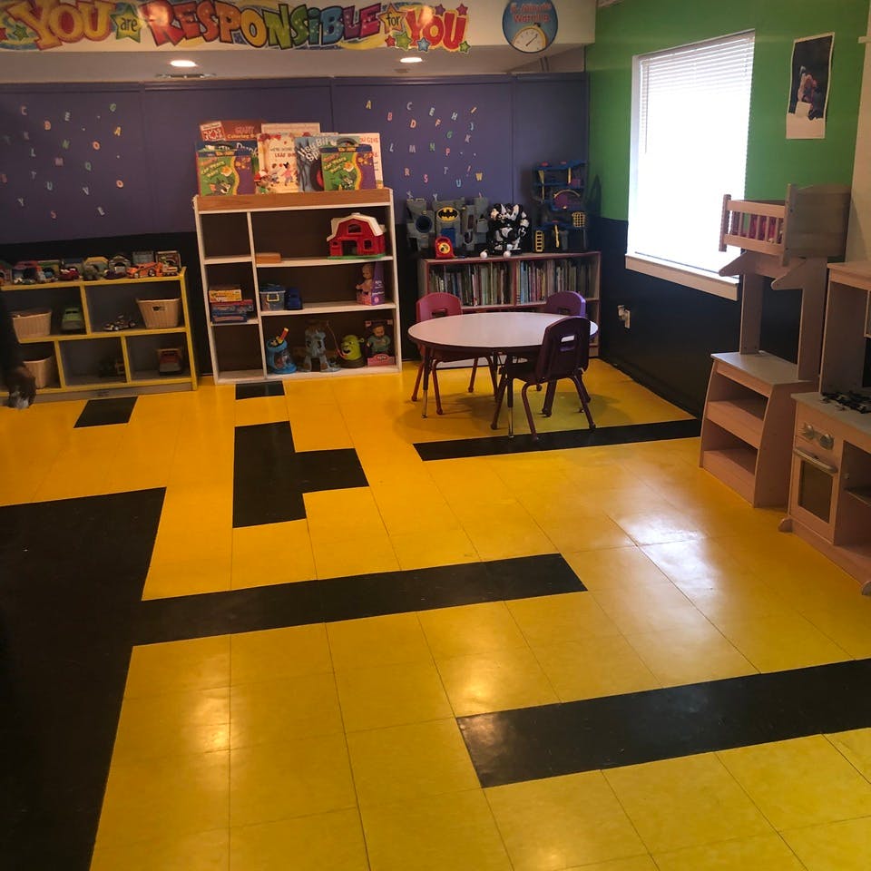 Classroom with yellow and black floor, shelves of books and toys, and small table