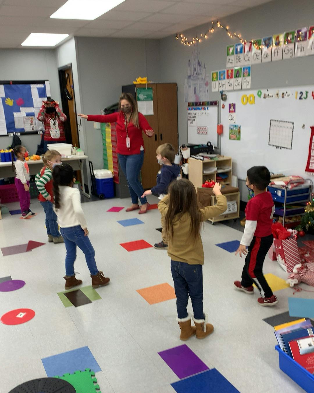 Adult and children standing on colorful shapes on the floor in a classroom