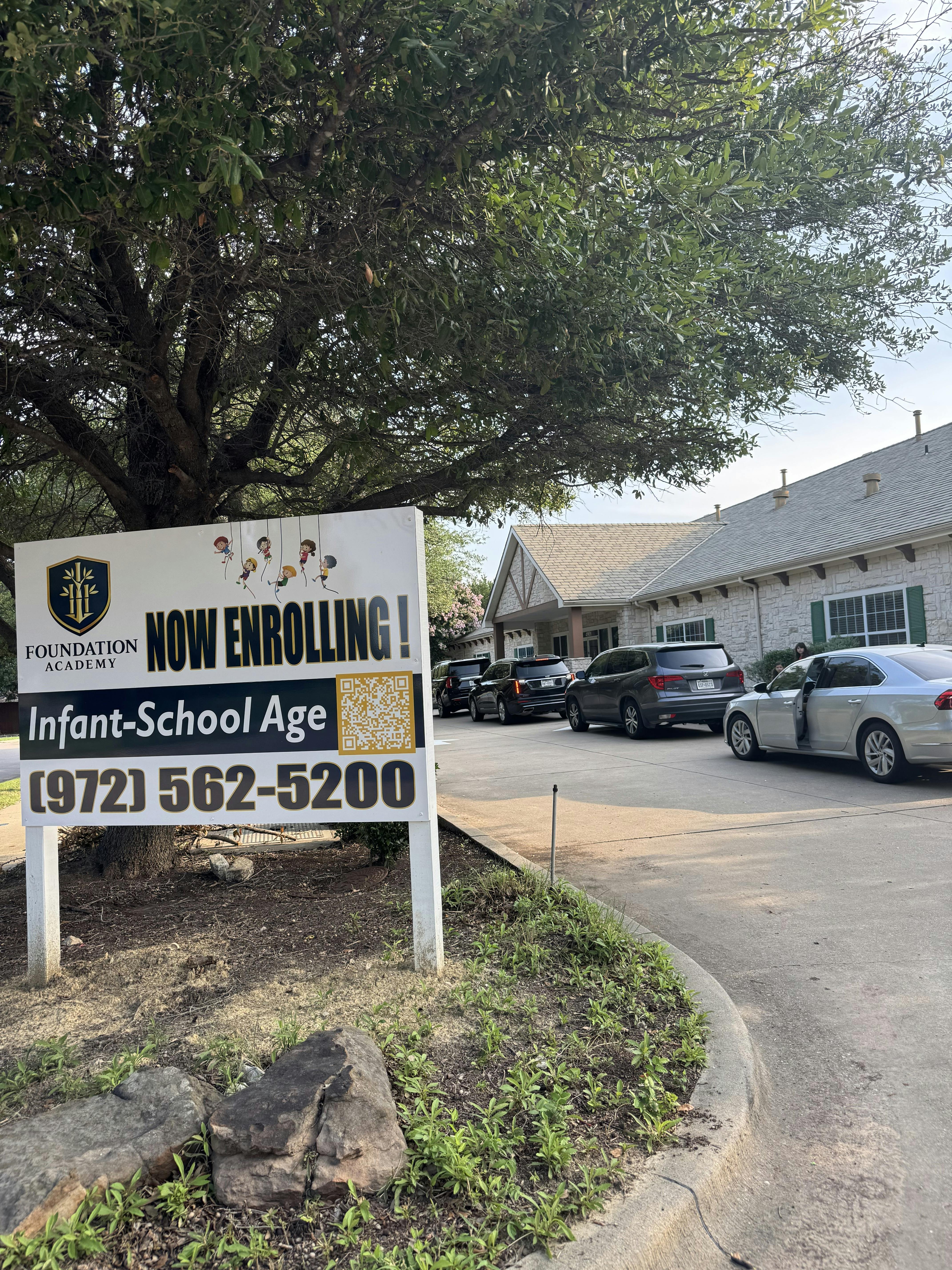 Foundation Academy enrollment sign in front of a school building with cars