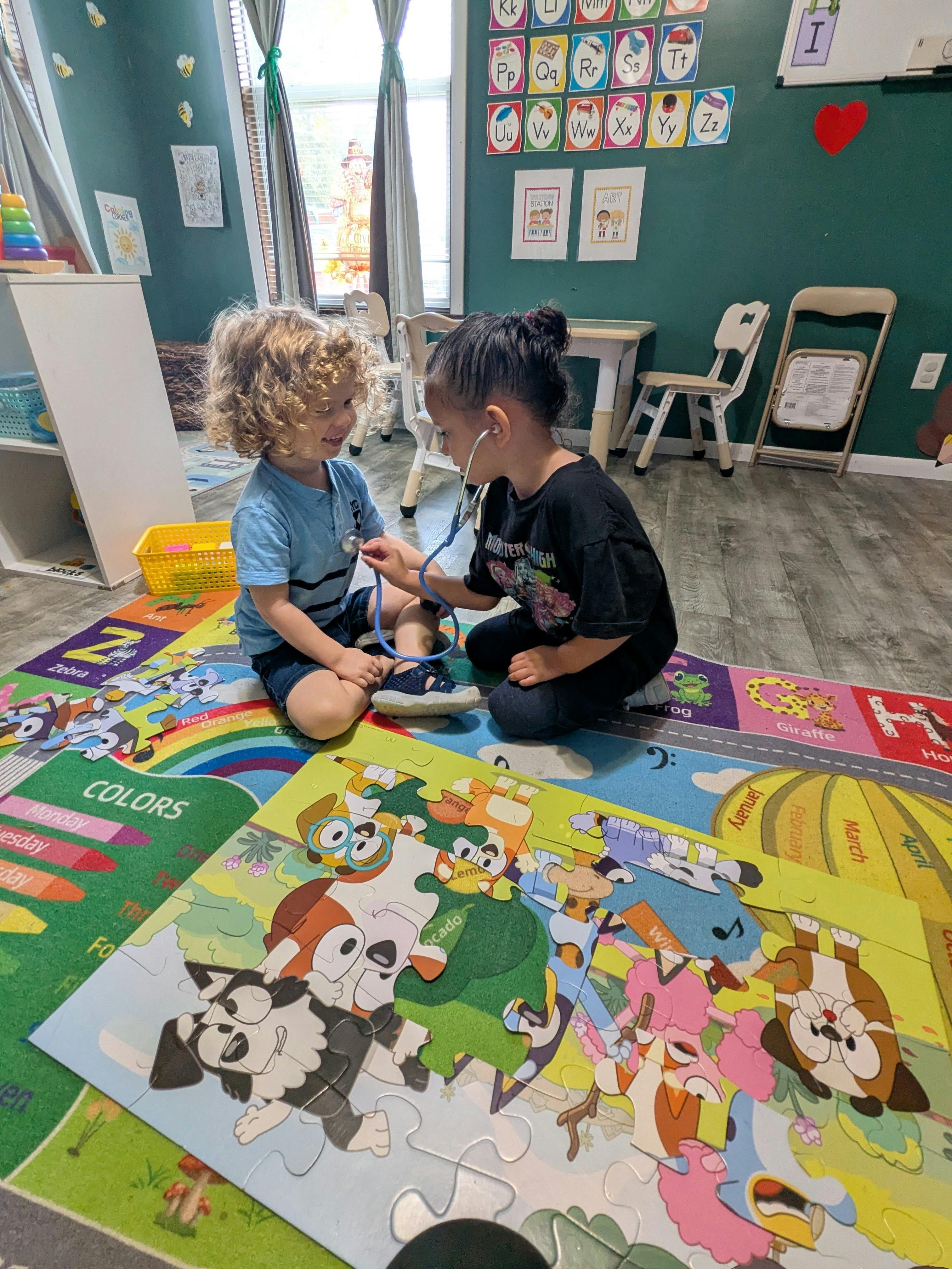 Two children playing with a toy stethoscope on a colorful rug in a classroom