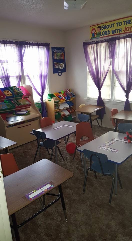 Classroom with small desks and chairs, toy shelves, and purple curtains