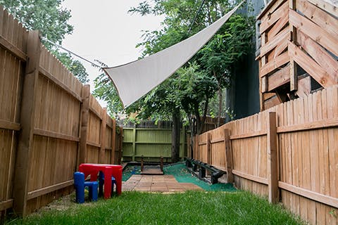 Backyard with wooden fences, a red table, blue chair, and a white sunshade